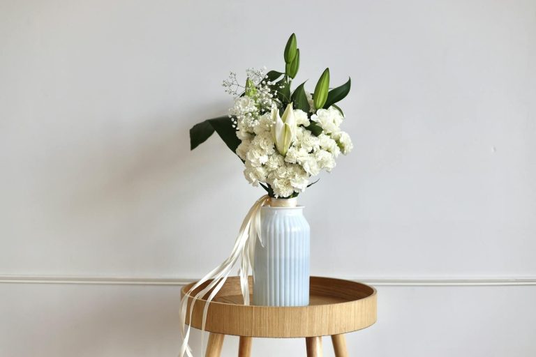 Stylish white flower bouquet in a blue vase on wooden stool, minimalist decor.