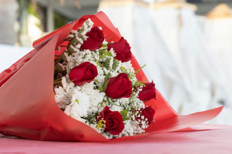 Beautiful bouquet of red roses and white flowers wrapped in vibrant red paper on a soft surface.