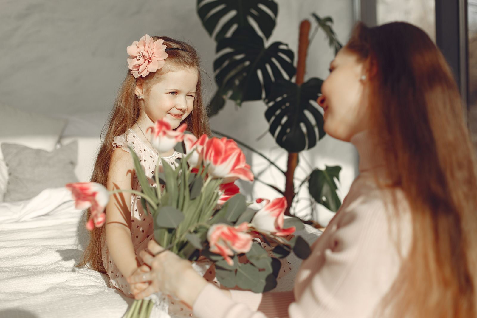 A joyful mother and daughter sharing a moment with tulips indoors, exuding happiness and love.