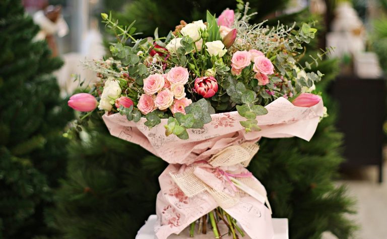 A beautiful floral bouquet with pink roses and tulips, wrapped in elegant paper, against a green background.